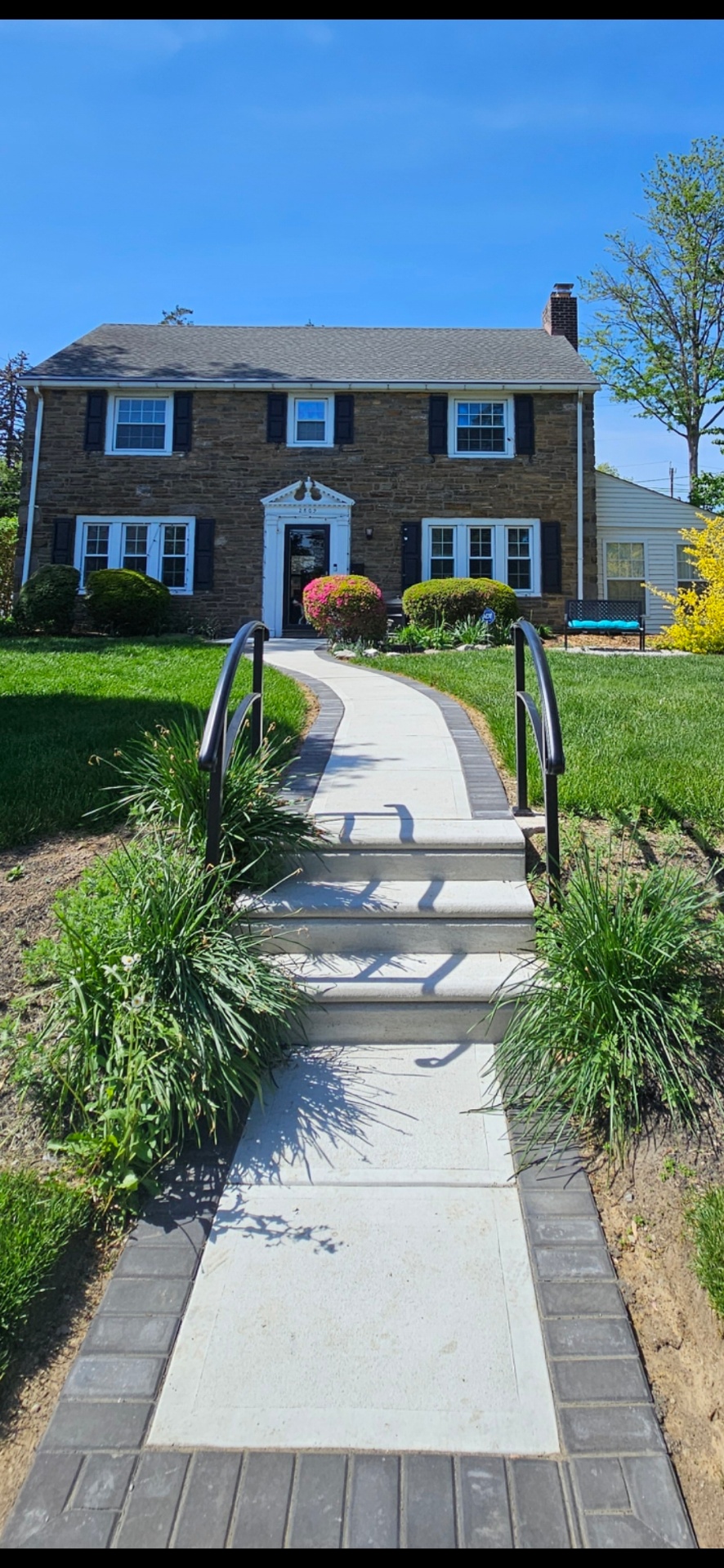 Concrete walkway with steps and paver border leading to stone home